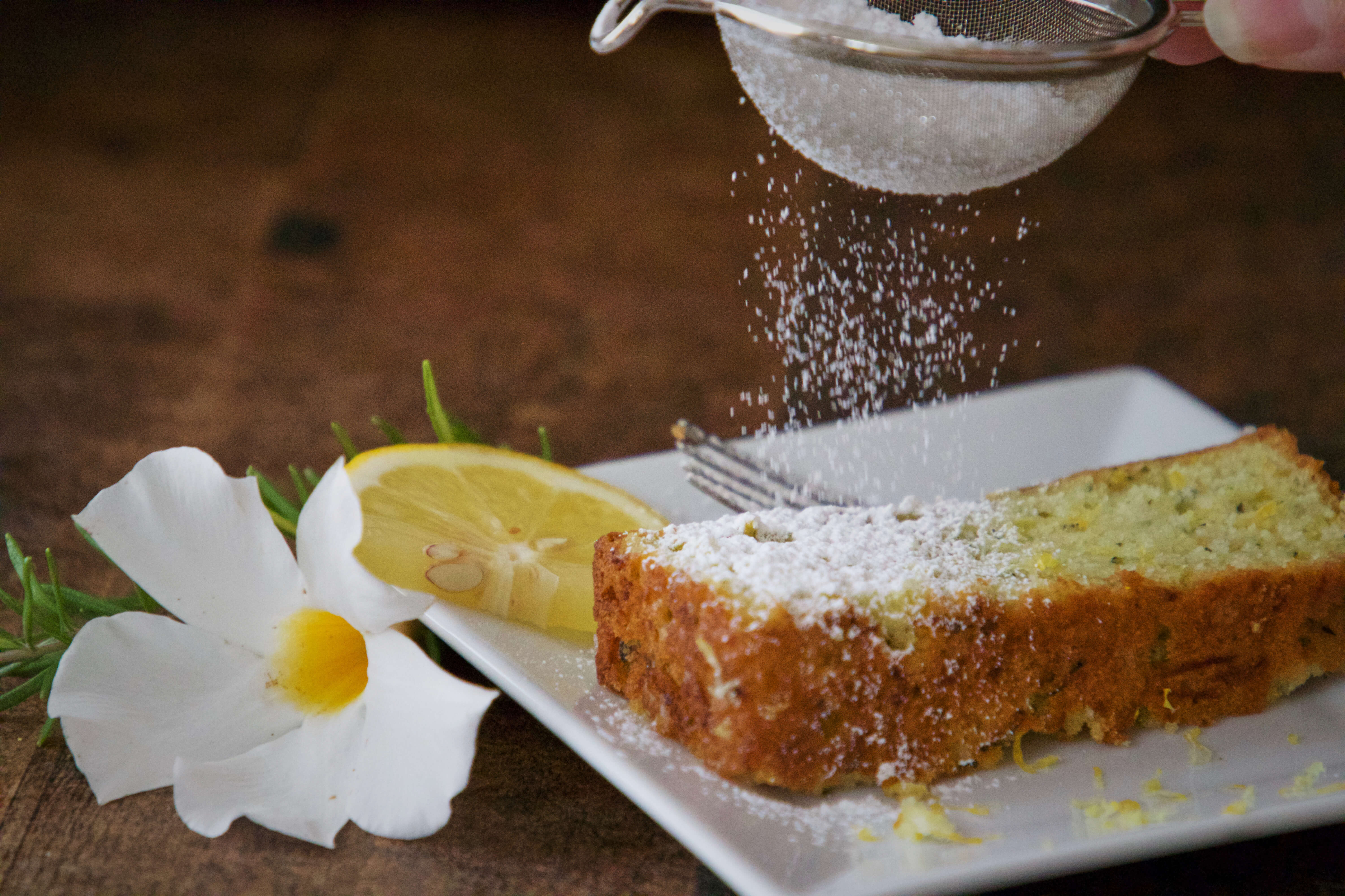 Somebody sprinkling icing sugar onto a slice of lemon loaf